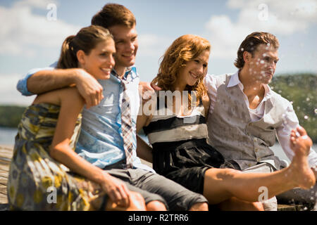 Gruppe von Freunden sitzen auf einem Steg, Planschen im See mit ihren Beinen. Stockfoto