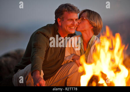 Lächelndes Paar mittleren Alters saß ein Lagerfeuer am Strand. Stockfoto