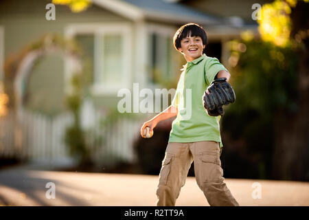 Lächelnde junge Junge spielt Baseball in einem vorstadtstraße. Stockfoto