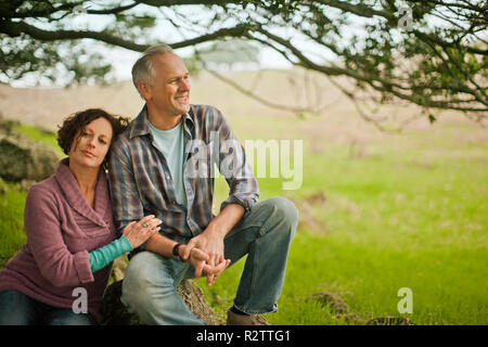 Paar mittleren Alters zusammen sitzen auf einem Felsen im ländlichen Bereich. Stockfoto