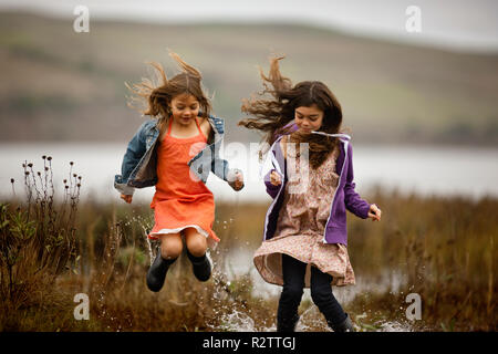 Zwei Mädchen lächeln, als sie springen und Spritzen in den Gewässern eines Sumpfes. Stockfoto