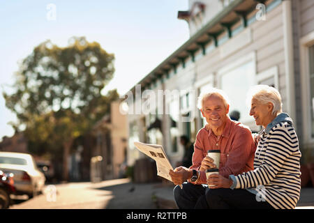 Lächelnd senior Paar sitzen eine Zeitung lesen und Kaffee trinken aus dem Becher zum Mitnehmen. Stockfoto