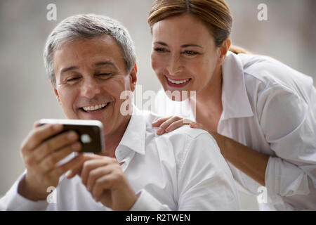 Paar mittleren Alters Lächeln, während bei einem tragbaren Gerät Informationen suchen. Stockfoto