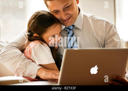 Mann auf seinem Laptop zu Hause arbeiten, mit seiner Tochter neben ihm. Stockfoto