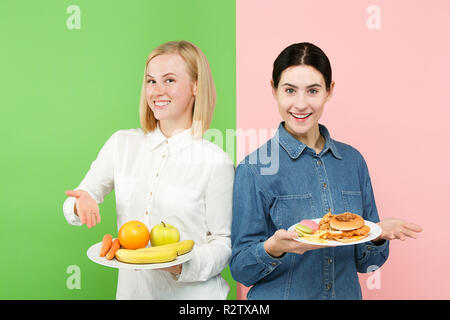 Diät. Diät Konzept. Gesunde nützlich Essen. Schöne junge Frauen die Wahl zwischen Obst und unhelathy Fast Food im Studio. Menschliche Gefühle und Vergleich Konzepte Stockfoto