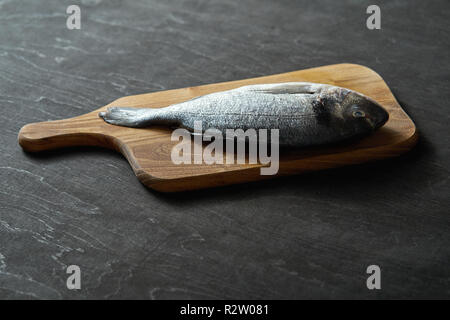 Eine rohe frische Fische Dorada auf einem Holzbrett und einem Schwarzen Tisch Stockfoto