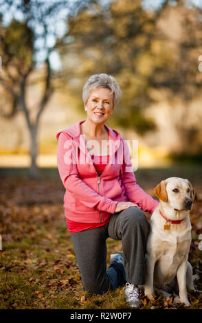 Porträt eines lächelnden älteren Frau in einem Park mit ihrem Hund. Stockfoto