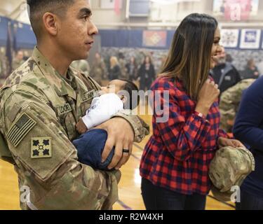 Staff Sgt. Michael Looney, der 2 Infantry Brigade Combat Team zugeordnet, 4 Infanterie Division, hält seine 7 Wochen alten Sohn, wie er mit seiner Familie vereint folgende Ein homecoming Zeremonie, William Bill Reed Special Event Center, Fort Carson, Colo., Nov. 13, 2018. Die 2 IBCT, 4. Inf. Div. Bereitgestellt im Februar nach Afghanistan die entschlossene Unterstützung der Durchführung von Zug, beraten und Maßnahmen, die es ermöglichen, der afghanischen nationalen Verteidigungs- und Sicherheitskräfte Sicherheit und Stabilität zu erhöhen, um die terroristischen sicheren Häfen zu verhindern, unterstützen. Zusätzlich ein Bataillon bereitgestellt für den Kosovo im s Stockfoto