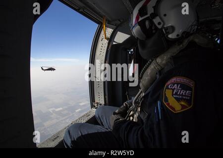 Tim Rodriguez, einem Militärhubschrauber Manager aus dem Kalifornien Abteilung der Feuer- und Forstwirtschaft (CAL FIRE), schaut aus dem Fenster eines UH-60M Black Hawk Hubschrauber über Bakersfield, Kalifornien, November 11, 2018, während in einem der beiden Kalifornien Army National Guard schwarzen Falken Position, der von den vereinten Kräften, Los Alamitos, im südlichen Kalifornien fliegt auf staatliche Agenturen Kämpfen der tödlichen Lagerfeuer in Nordkalifornien unterstützen. CAL FIRE Aircrew Mitglieder melden Sie Kalifornien Nationalgarde Helikopter Besatzungen während wildfire Missionen Feuer Wissen an die Crew hinzuzufügen und dienen als Bindeglied zwischen Stockfoto