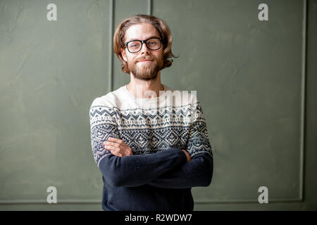 Portrait einer jungen bärtigen Mann mit langen Haaren in Pullover auf der grünen Wand Hintergrund drinnen gekleidet Stockfoto