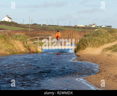 Eine Frau in der hellen Jacke und ein Mops stehend auf einer Brücke an der Kamera in Rhosneigr, Anglesey, Wales, Vereinigtes Königreich, Stockfoto