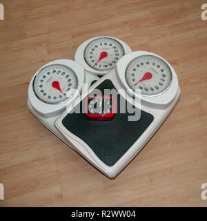 Diät, Gewichtsverlust und Körperbild konzeptionelle Bild von drei analogen Waage eine auf der anderen mit einer Uhr für Dringlichkeit gestapelt Stockfoto