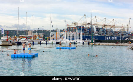 KOPER, Slowenien - 24. Juli 2014: Ein paar Badegäste in den Gewässern vor der Hafenstadt, mit einem großen Container schiff im Hintergrund Stockfoto