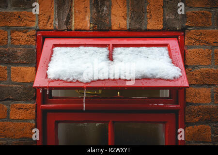 Ein rot eingerahmten Fenster mit Schnee und Eiszapfen mit einer Mauer im Hintergrund. Querformat. Stockfoto