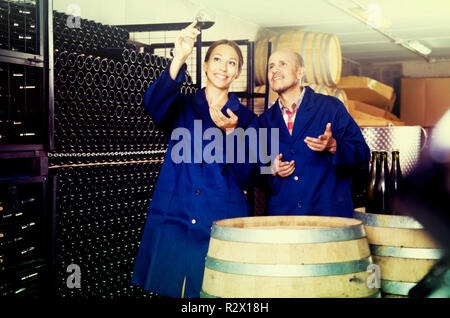 Froh, dass Mann und Frau Mitarbeiter bei Wein im Glas stehen in Weinkeller suchen Stockfoto