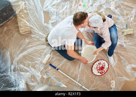 Glückliches Paar küssen, während der Renovierung beim Malen im neuen Haus Stockfoto