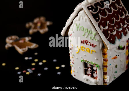 Auf einem schwarzen Hintergrund ein weißer Lebkuchen Haus mit einem braunen Dach ist, einem Fenster und die Inschrift Frohes Neues Jahr auf einer weißen Wand und mit multi-color Stockfoto