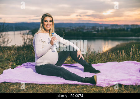 Schöne schwangere Frau genießt Trinkwasser während der Zeit im Freien. Stockfoto