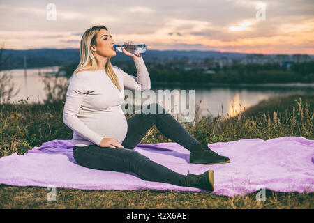 Schöne schwangere Frau genießt Trinkwasser während der Zeit im Freien. Stockfoto