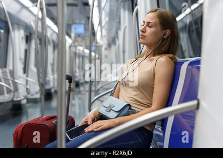 Müde junge Frau mit roten Koffer in der U-Bahn sitzen Stockfoto