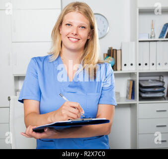 Lächelnd weibliche Krankenschwester in formale Abnutzung Registrierung Informationen in Form Stockfoto