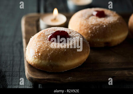 Nahaufnahme von einigen sufganiyot, jüdische Krapfen gefüllt mit Strawberry jelly traditionell gegessen auf Hanukkah, und einige Kerzen, auf einem rustikalen Holztisch Stockfoto