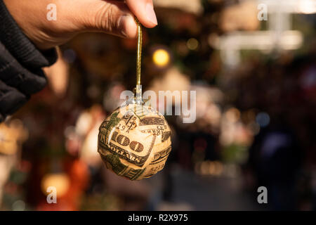 Nahaufnahme von einem jungen Mann mit einem christmas Ball auf Stücke von uns 100 Dollar Bill in einem Weihnachtsmarkt gewickelt Stockfoto