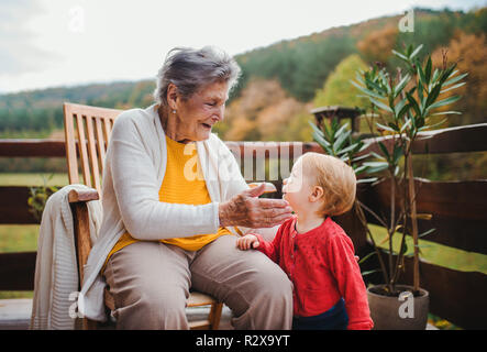 Ältere Frau sitzend mit einem Kleinkind Urenkel auf einer Terrasse im Herbst. Stockfoto