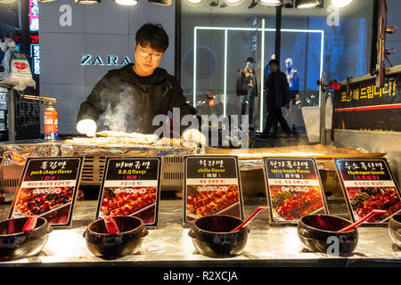 Eine Street Food standbesitzer Köche gegrilltem Schweinefleisch Kebabs auf seinem Stall in Myeongdong in Seoul, Südkorea Stockfoto