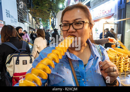 Eine Dame isst eine tiefe feuerte Kartoffel Spirale auf einem Stock eine Straße Garküche in Myeongdong in Seoul, Südkorea Form gekauft. Stockfoto