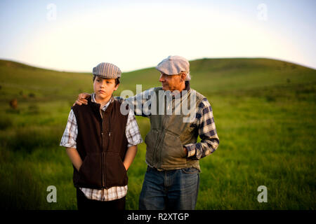 Teenager und sein Großvater ein Gespräch während zusammen gehen über eine Wiese auf einem Bauernhof. Stockfoto