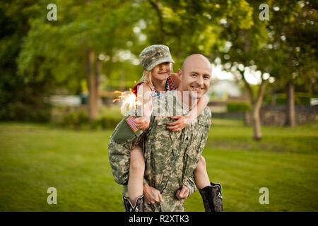 Lächelnd männlichen Soldaten piggy-backing seine junge Tochter in ihrem Hinterhof. Stockfoto