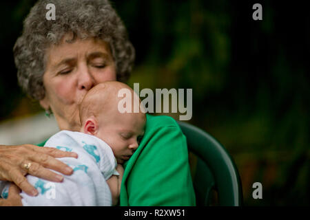 Ältere Frau sitzt und halten ein neugeborenes Baby in einem Hinterhof. Stockfoto