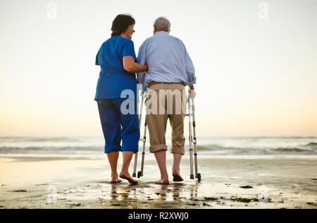Älterer Mann mit einer Gehhilfe neben einem weiblichen Krankenschwester am Strand. Stockfoto