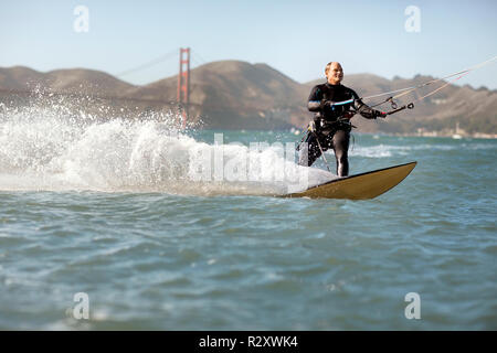 Mitte der erwachsene Mann Kitesurfen in der Nähe der Golden Gate Bridge, San Francisco, USA. Stockfoto