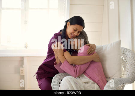 Lächelnd weibliche Krankenschwester, die eine ältere Patientin in einem Sessel. Stockfoto