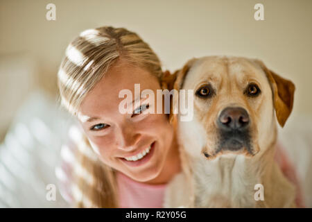 Lächelnden jungen Frau umarmt sie Hund in Ihrem lichtdurchfluteten Schlafzimmer. Stockfoto