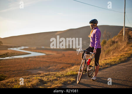 Junge Frau nimmt einen Bruch von unten Radfahren eine Landstraße, um die Landschaft zu bewundern. Stockfoto
