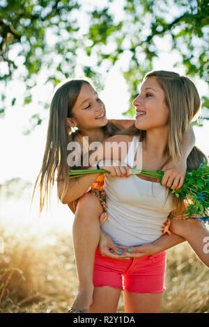 Lächelnd Jugendmädchen ihre jüngere Schwester, die auf ihrem Rücken. Stockfoto