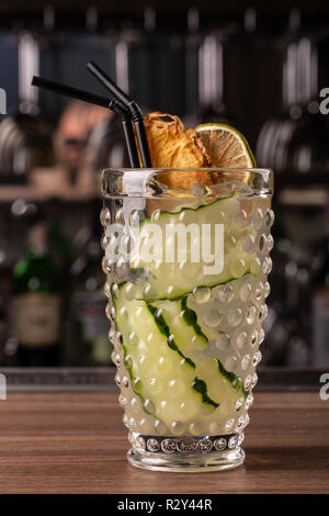 Glas Gin Tonic Cocktail mit Gurke am Hieb gegen den Hintergrund eingerichtet. Cocktail an der Bar Stockfoto