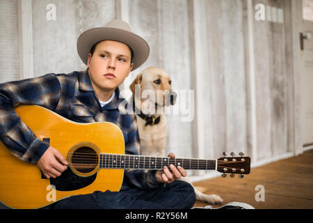 Teenager spielen eine Akustik Gitarre mit seinem Hund. Stockfoto