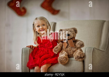 Junges Mädchen sitzt auf einem Sessel mit ihrem Teddybär. Stockfoto