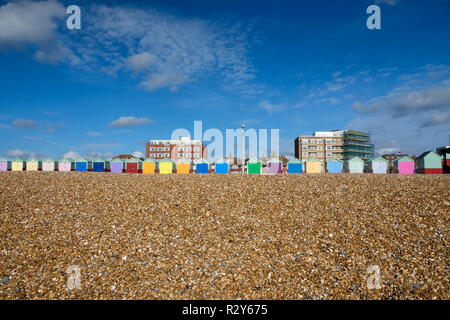 Im Vordergrund ist ein Kieselstrand, eine Linie von 20 drei bunten Badekabinen in der Mitte über ihnen sind ist ein blauer Himmel mit weißen Wolken der Su Stockfoto