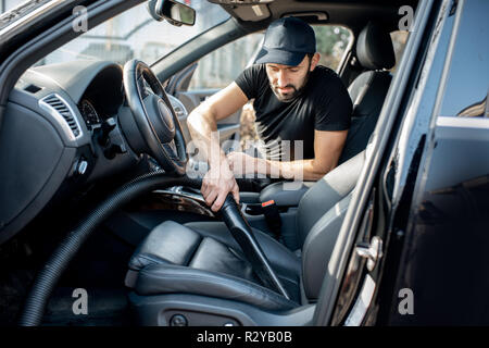 Professionelle Reinigungsmittel in schwarzen T-Shirt und Cap staubsaugen Ledersitze eines Luxuswagens Stockfoto