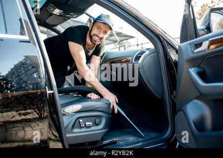 Porträt eines professionellen Reiniger in schwarzen T-Shirt und Cap staubsaugen Matten eines Luxuswagens Stockfoto