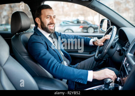 Schöne bärtige Geschäftsmann im Anzug, der ein Auto fährt in der Stadt angezogen Stockfoto