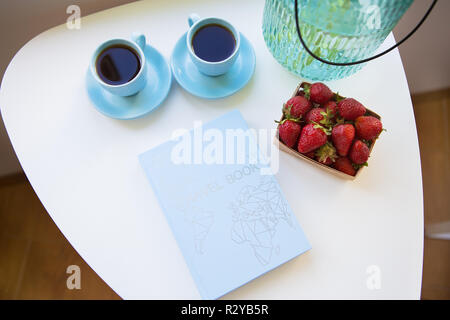 Erdbeere, Buch, Strauß Pfingstrosen und zwei Tassen Kaffee auf weißer Tisch. Stockfoto