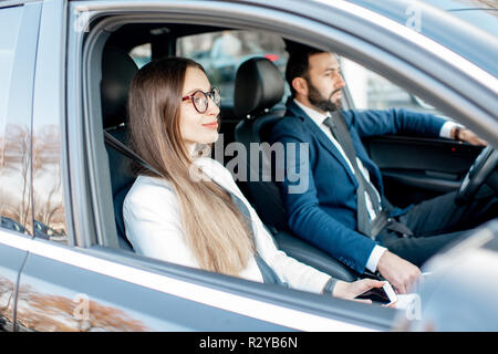 Kaufmann und Frau gekleidet in den Anzügen fahren Luxusauto, Blick von außen durch die Fenster Stockfoto