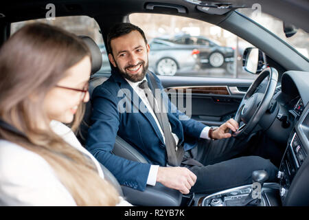 Happy Geschäftsmann und Frau gekleidet in die Anzüge zusammen gesprochen während der Fahrt ein luxuriöses Auto in der Stadt Stockfoto