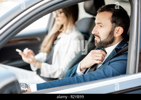 Elegante Geschäftsmann Anziehen der Riegel während der Fahrt ein Auto mit geschäftsfrau Stockfoto